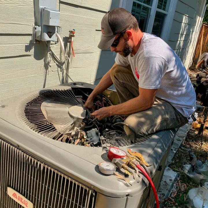 Technician working on an open condenser fan assembly with pressure gauges nearby